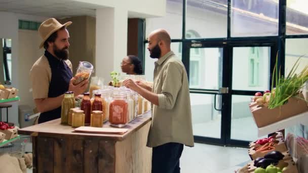 食料品のためのビーガン顧客のショッピングにオーガニックアイテムを提示する商人 容器にソースやパントリーグッズを示す 新鮮な自然食品を購入することを考えるクライアント — ストック動画