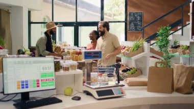 Satıcı markette müşteriye yardımcı oluyor, taze toplanmış meyve ve sebzeleri sergilemeyi öneriyor. Yerel sıfır atık süpermarketinde organik ekolojik ürün arayan çift.