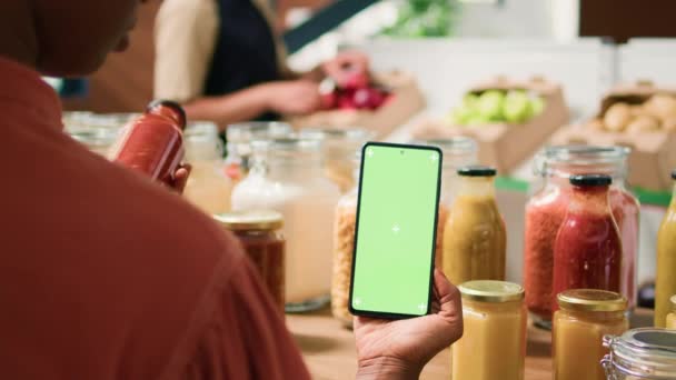 非裔美国人客户在寻找可重复使用的罐子中的有机生态大宗产品时使用绿色屏幕 女顾客用孤立的铬钥匙模拟显示屏检查智能手机 — 图库视频影像