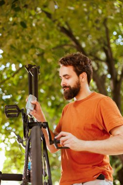 Yıllık yaz bakımı için modern bisiklet zincirini yağlayan ve hizmet veren odaklanmış ve aktif bir adam. Açık havada bisiklet pedallarını ustalıkla kayganlaştıran beyaz bir erkek görülüyor..