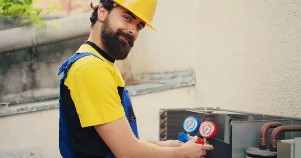 stock image Efficient technician looking at refrigerant levels in external air conditioner while using manifold meters to precisely measure the pressure in HVAC system, ensuring efficient cooling performance