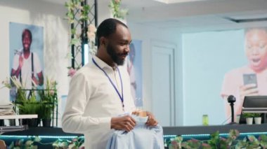 Personel raflarda lüks moda butik şık kıyafetler stokluyor. Afro-Amerikan işçiler moda giyim mağazasında askılara üst sınıf erkek gömlekleri ve diğer giysiler ekliyorlar.