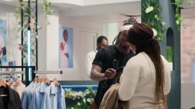 Süslü moda butiği içinde Afrikalı Amerikalı bir adam onun giymesi için ideal şık kıyafetler deniyor. Premium Showroom 'daki müşteri kız arkadaşının uygun kıyafet koleksiyonunu bulmasına yardım etti