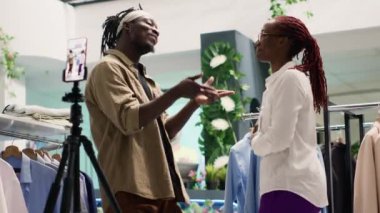 SH giyim mağazasının içerik yaratıcısı müşterileri cezbetmek için yardımcı indirimler sunan esnafın videosunu çekiyor. Sosyal medya takipçileri için indirimli mağaza kaydında medya yıldızı ve perakende yardımcısı