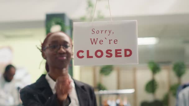 アフリカ系アメリカ人の従業員が午前中に衣料品店を開設し 顧客を待っている ショッピングセンターのファッションブティックドアに閉じたメッセージサインを回すBipoc小売労働者 — ストック動画