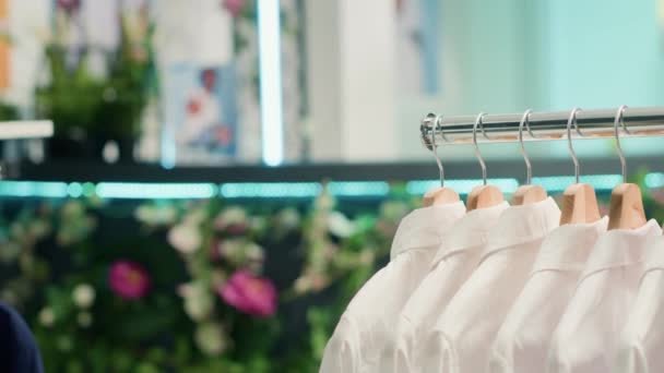 ショッピングセンターの無駄なショッピングアウトレットゼロから安価で持続可能な衣料品のパンニングショット エコフレンドリーなセカンドハンドストアでエレガントな白い結婚式の男性のシャツのクローズアップショット — ストック動画