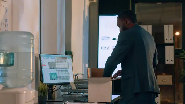 Employee upset by company manager, leaving office after deciding to quit, being consoled by thoughtful coworker. African american businessman packing desk belongings before starting another job