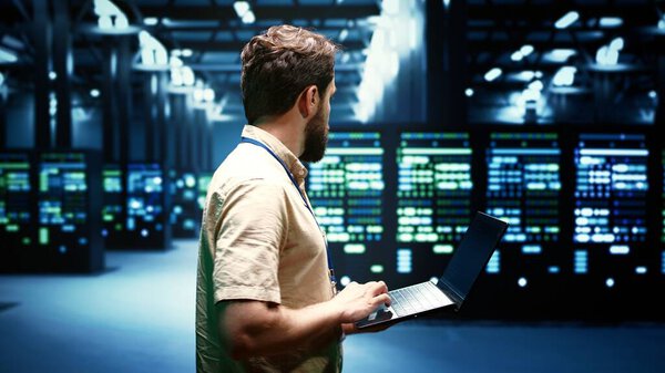 Administrator checking event logs and diagnostic tools to identify malfunctioning data center equipment root cause. Engineer using laptop to inspect server rig operating system configuration settings