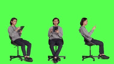 Çevrimiçi internet sitesinde arama yapmak için mobil cihaz kullanan Asyalı adam yeşil ekran şablonu üzerinde tarayıcıda geziniyor. Genç yetişkin sandalyede oturuyor ve tablet üzerinde çalışıyor, rahat bir adam..