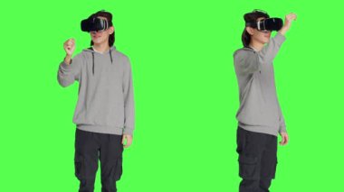 Stüdyoda yeşil ekranlı sanal gerçeklik aleti kullanan bir erkek, interaktif 3D kulaklıkla eğleniyor. Modern Asyalı adam yapay zekanın tadını çıkarıyor..