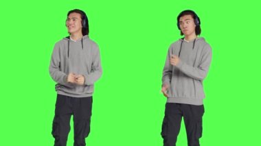 Erkek model müzik dinliyor ve müzik kulaklıklarıyla stüdyoda dans ediyor, şarkılarla ve dans hareketleriyle eğleniyor. Neşeli insan iyimser ve havalı, yeşil ekran.