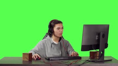Asyalı bir yetişkin iş yerinde arkadaşlarıyla online RPG oyunları oynuyor. Genç adam yeni web yarışmasında eğleniyor, yeşil ekran arka planında kulaklık takmış insanlarla konuşuyor..
