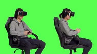 Oyuncu, başlık ve kumandayla eğleniyor, başkalarıyla online oyun oynuyor. Asyalı biri yeşil ekran arka planına karşı sandalyede otururken boş vakitlerin tadını çıkarıyor..