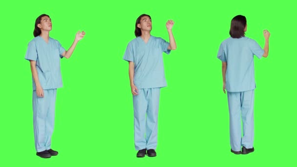 アジアの医療看護師は グリーンスクリーンデザインのスタジオでホログラムをチェックし ホログラフィックアイコンタブと人工知能を使用しています 医療の専門知識を持つユニフォームの男性スペシャリスト — ストック動画