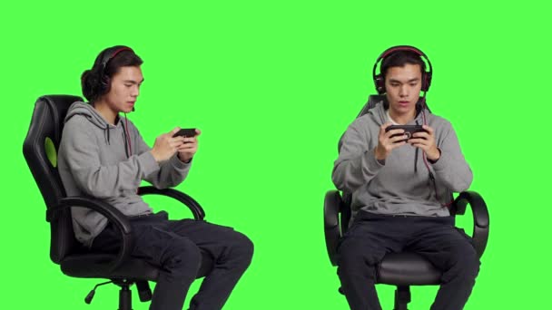 Azjatycki Młody Człowiek Gra Gry Mobilne Zielonym Ekranie Trzymając Smartfona — Wideo stockowe