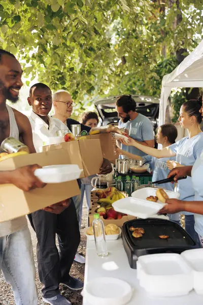 Volunteers provide meal boxes and canned goods to needy individuals. Seniors and homeless people receive nourishment from smiling workers embodying spirit of food drive and non-profit organization.
