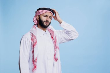 Geleneksel giysiler içinde yorgun düşmüş Müslüman adam migrenden acı çekerken başını tutuyor. Yorgun bir Arap 'ın başörtüsü ve başörtüsü takması başını ağrıtıyor.