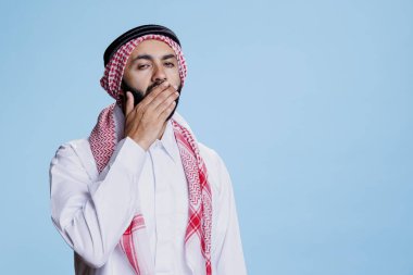 Geleneksel giysiler içinde yorgun Müslüman adam esniyor ve uykulu bir ifadeyle kameraya bakıyor. Yorgun arap adam eliyle ağzını kapatıyor, sıkılmış jestler yapıyor.