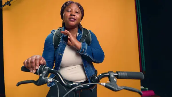 Video showcasing african american bike messenger happily explaining about her courier service job. Young black woman on bicycle talking to camera about food delivery service. Handheld shot.