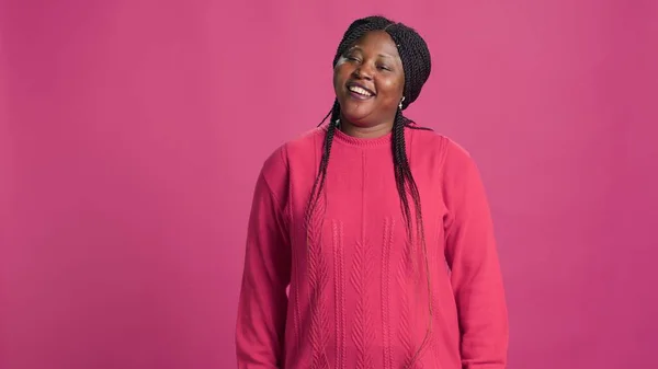 Video captures trendy african american beauty embracing pink sweater fashion, posing confidently against vibrant background. Black woman chuckling adding authentic touch to photo shoot.