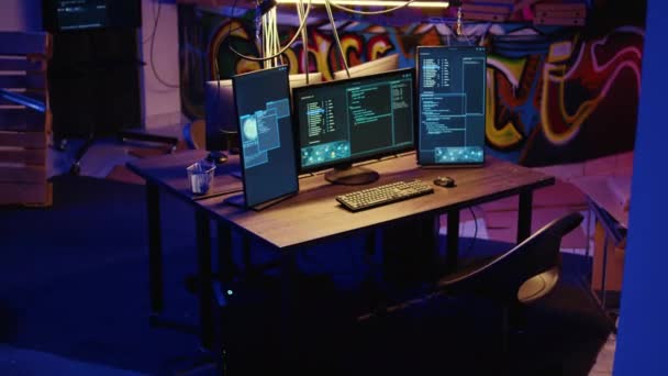 空の倉庫で悪意のあるコードを実行する高度な技術コンピュータシステムのジブダウンショット ハッカーが不正行為を行うために使用する地下隠れ家を描いた空のグラフィティのPcモニター — ストック動画
