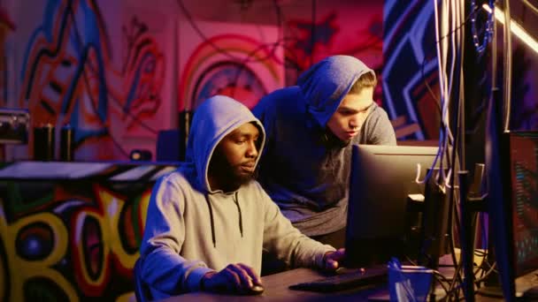 ハッキンググループの新しいメンバーは 隠れたベースで彼のメンターとして機能する知識のある不正プログラマーからのガイダンスを受け取ります アフリカ系アメリカ人のハッカーがスクリプトキディにコンピュータをハッキングする方法を教える — ストック動画