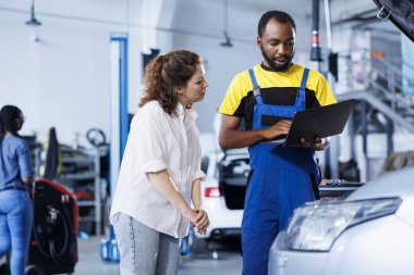 Repairman at auto repair shop conducts yearly vehicle checkup, informing customer about needed engine mending. BIPOC garage worker discussing with customer after finishing car maintenance clipart