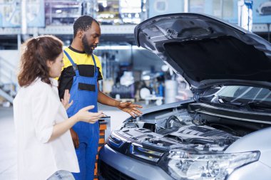 Afro-Amerikan tamirci araba tamirhanesinde müşteriye yardım ediyor. Garaj çalışanı kadınla otomobil parçalarına bakıyor, teftiş sırasında aracının motorunu tamir ediyor.
