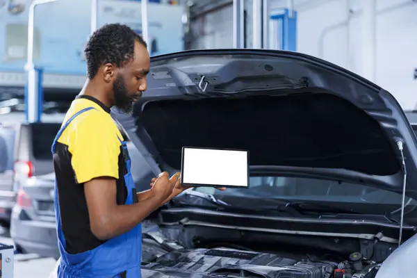 African american mechanic trainee uses mockup tablet in car service to watch tutorial on how to replace motor. Garage workplace intern looks up training videos online on isolated screen device