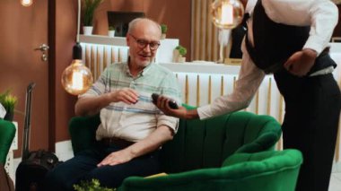Yaşlı adam kredi kartıyla ödeme yapıyor. Otel lobisinde beklerken bardan içki almak için elektronik ödeme yapıyor. Çiftle uluslararası tatilde olan yaşlılar konsepti.