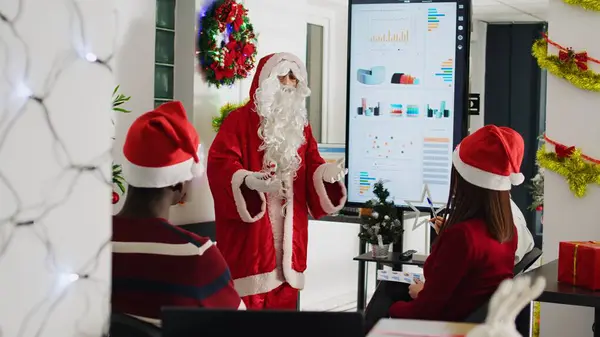 有执照的演说家穿着圣诞老人的服装 在公司员工面前用棒棒糖做演示 工作人员在圣诞华丽的办公室里学习如何提升自己的事业 — 图库照片