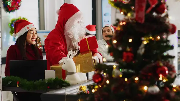 多族裔工人接受同事们的礼物 假装圣诞老人在圣诞装饰办公室里 在寒假期间 穿着服装的员工给公司人员带来了惊喜 — 图库照片