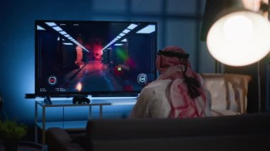 Uzun bir iş gününden sonra TV 'de video oyunu oynayan adam, ekranda geri çekildikten sonra kızgın bir şekilde oyun oynuyor. Müslüman oyuncu, oyun konsolu bilim kurgu atıcısı yarışmasını kaybettikten sonra sinirlendi