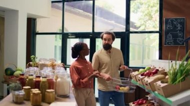 Satıcıya organik sıfır atık mağazasında taze ürünler hakkında soru soran çift, mağaza sahibi bahçeden toplanan meyve ve sebzeleri tavsiye ediyor. Kimyasal madde tüccarları bedava yemek sunar..