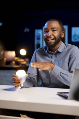 Afro-amerikan etkileyicisi ampulün farklı renklere dönüşebildiğini filme alıyor. Teknoloji meraklısı ses komutları tarafından kontrol edilen akıllı ev otomasyon teknolojisi sergiliyor