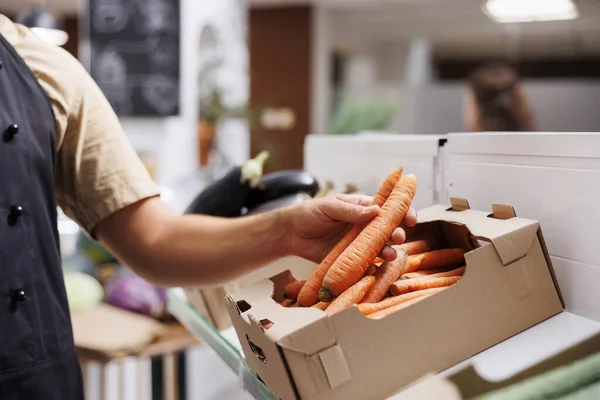 Trader fills up crates on low carbon footprint zero waste shop shelves with locally grown vegetables. Storekeeper restocks local groceries store with food items, close up shot on carrots