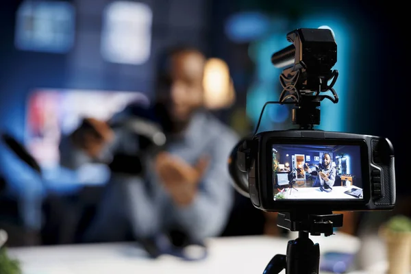 Focus on professional video production gear used for capturing footage of internet show host in blurry background filming tech reviews for his online channel, showcasing stereo headphones