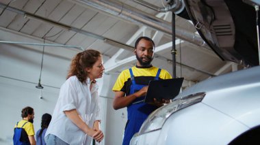 Araba servisi lisanslı mühendisi, motoru değiştirdikten sonra vidaları sıkmak için iş istasyonundaki banktan tork anahtarı seçiyor. Afrikalı Amerikalı garaj işçisi müşteri otomobilini tamir ediyor