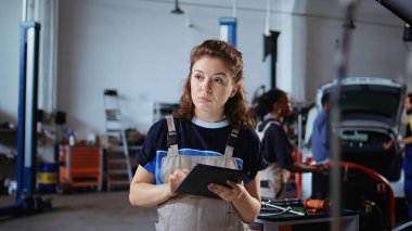 Teftiş sırasında araba performans parametrelerini kontrol etmek için tablet kullanan neşeli bir mühendis. Rahatlamış garaj işyeri çalışanı hasarlı aracı incelemek için aygıt kullanıyor