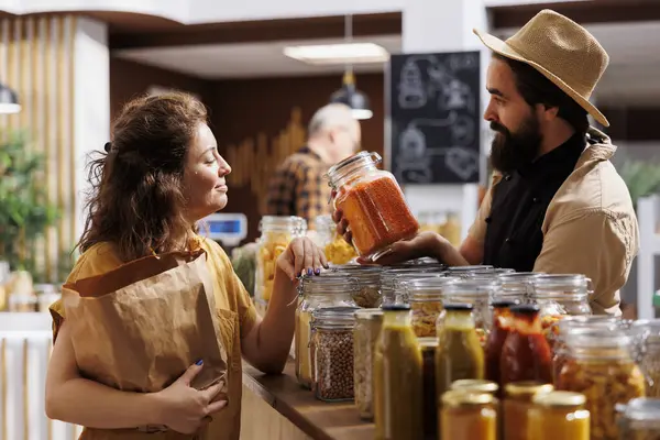 Zero waste shop entrepreneur showing his natural chemical free products to customer interested in low planet impact lifestyle. Ecofriendly supermarket owner presenting his merchandise to client