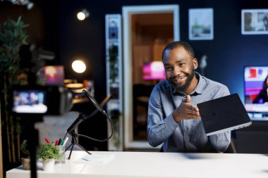 Afro-Amerikan internet şovu sunucusu profesyonel kamera ve mikrofon kullanarak yılın en iyi oyun dizüstü bilgisayarlarını filme alıyor. Teknik mühendis not defteri dijital aygıt incelemesi kaydediyor