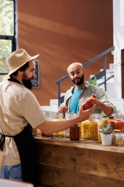 Satıcı, vejetaryen müşterilere yiyecek alışverişi için organik ürünler sunuyor. Konteynırlarda sos ve kiler var. Müşteri taze doğal gıda ürünleri almayı düşünüyor..