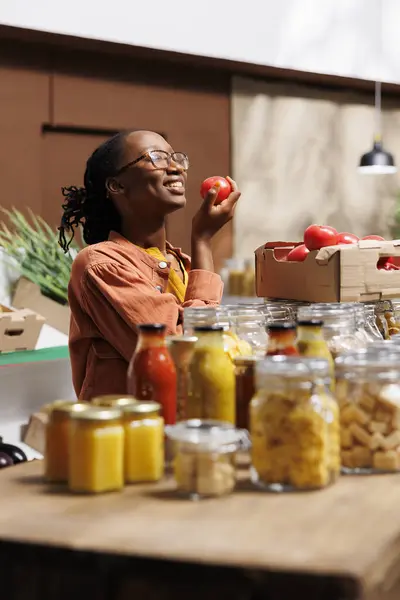 stock image Selective focus on black woman at zero waste store smelling organic farm-grown tomato. African American female customer at local market enthusiastically admires freshly harvested produce.