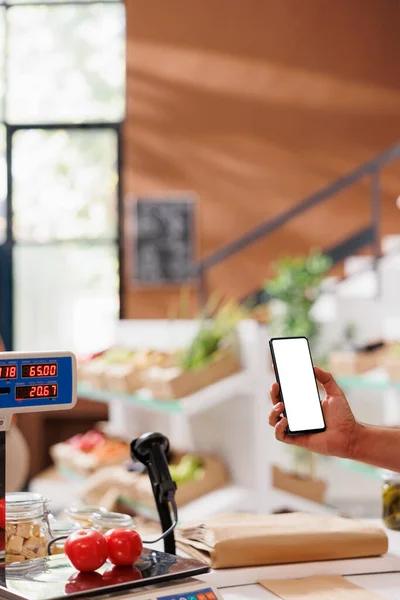 Shopkeeper analyzing locally grown produce with a mockup mobile phone. Smartphone with isolated white screen, male seller thoroughly checks local supermarket food items for allergens.