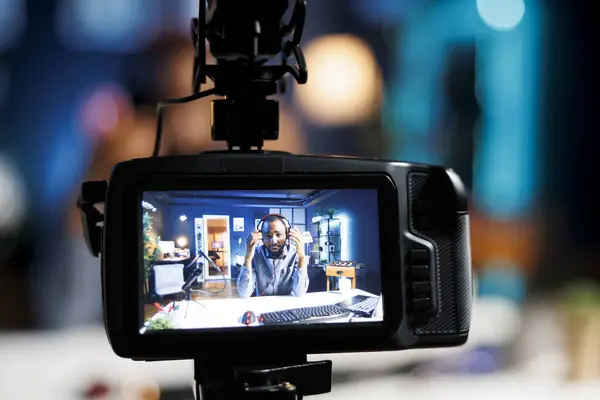 Focus on professional video production gear used for capturing footage of content creator in blurry background filming tech reviews for his internet channel, showcasing pair of headphones