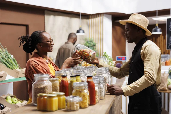 友好的非洲裔美国男性小贩建议和帮助黑人妇女新鲜的面食建议 这家商店提供有机产品 大宗商品和无塑料包装 — 图库照片