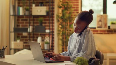 Teleworker evde blog makaleleri üzerinde çalışırken telefonla konuşuyor, iş ile ilgili bazı sorunları çözmek için editörle konuşuyor. Gelişim için telefon hattını kullanan Afrikalı Amerikalı..