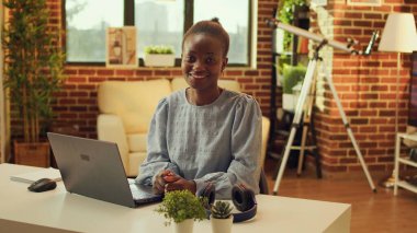 Masadaki Afrikalı Amerikalı tele-işçi gün batımında güzel aydınlatılmış bir odada online görevler üzerinde çalışıyor. Freelancer evde uzaktan çalışıyor, blog yazıyor ve e-posta gönderiyor. Çoklu Görev.