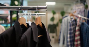 Kamera görüntüsü, yeni koleksiyonun modaya uygun kıyafetlerini sergileyen üst düzey tasarımcı sergi salonundaki askıların üzerindeki tişörtlerden oluşan şık bir seçimle seyahat ediyor. Erkek kıyafetleriyle dolu alışveriş merkezi moda koridorları.