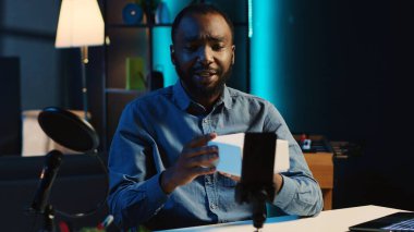 Teknoloji içeriği üreticisi paketlenmiş ürünleri boks olmadan filme alıyor ve satın almak için nedenler sunuyor. Influencer video kaydı aboneleri prodüksiyon teknolojisi kullanarak sponsor ortak ürünleri satın almaya teşvik ediyor